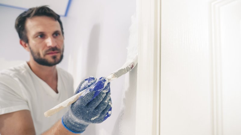 Man cutting in white paint around door frame with paint brush (Photo by RightFramePhotoVideo - stock.adobe.com)